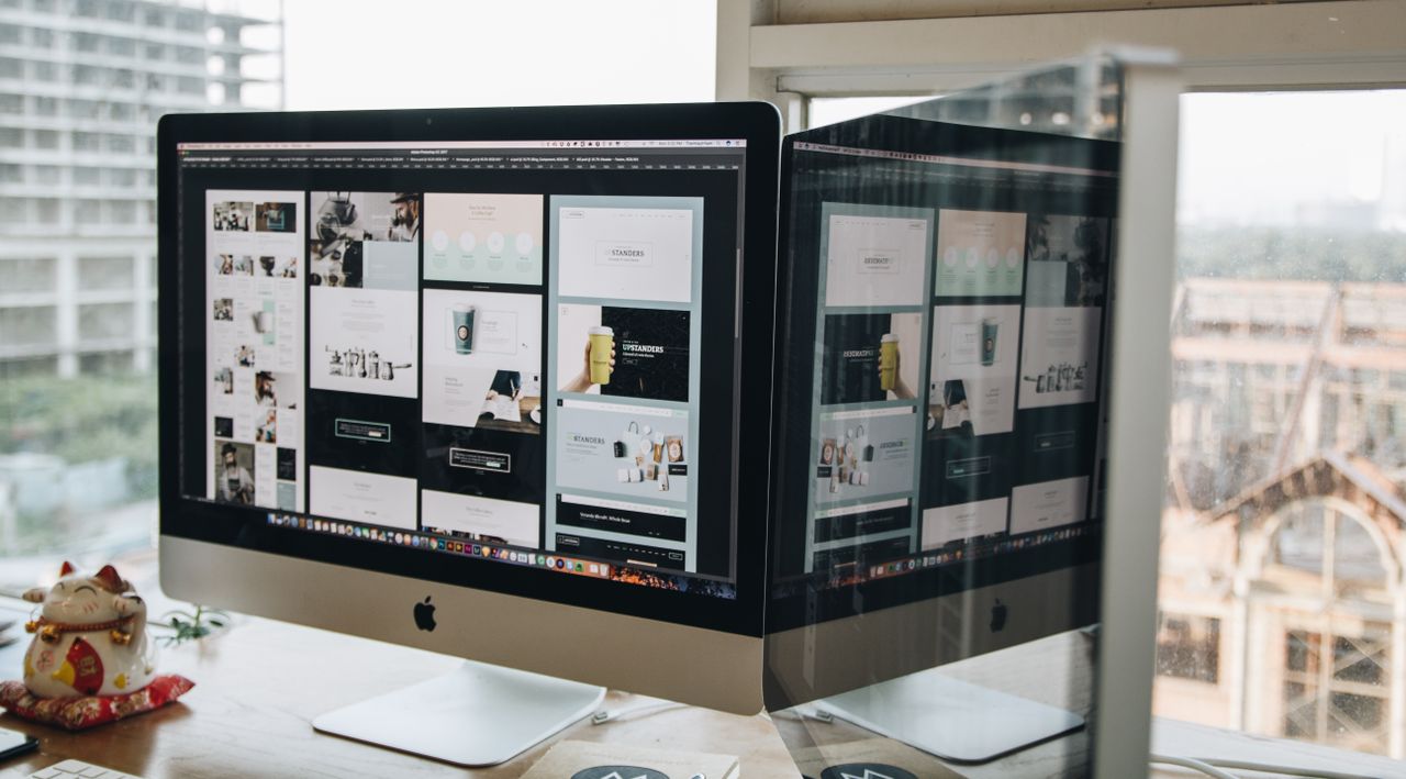 services-02 Dual monitors on a desk, showcasing web design in a modern office setting.